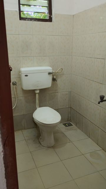 Tiled bathroom with western toilet at Ashraf Gents Hostel, Kalamassery